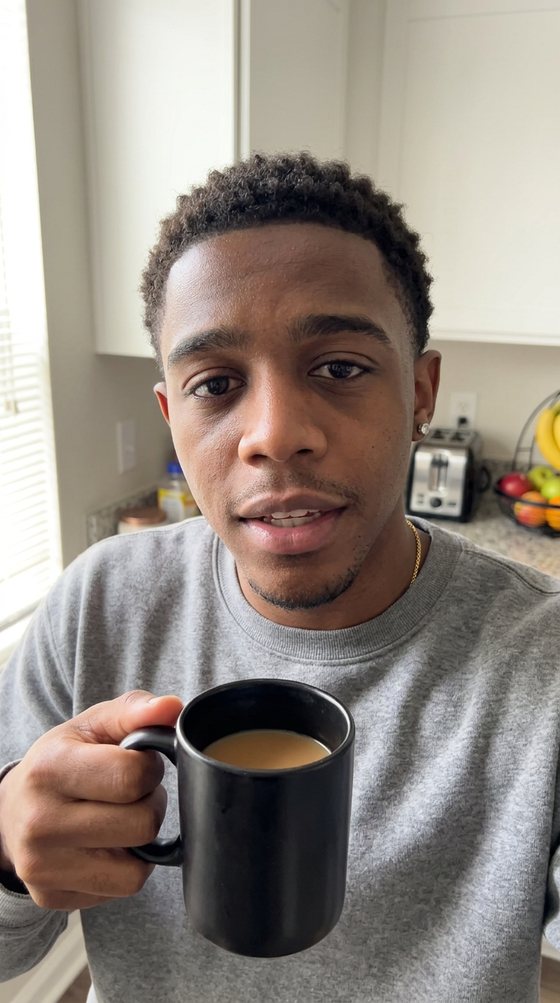 AI-generated creator image: Marcus in a sunlit kitchen holding a coffee toward the phone camera, mid-sentence, Monday morning