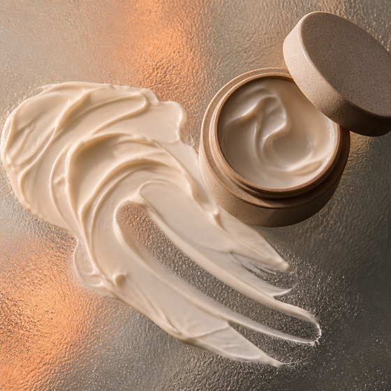 AI-generated ad image: a thick swirl of white face cream smeared on frosted glass beside an open matte jar, warm side light