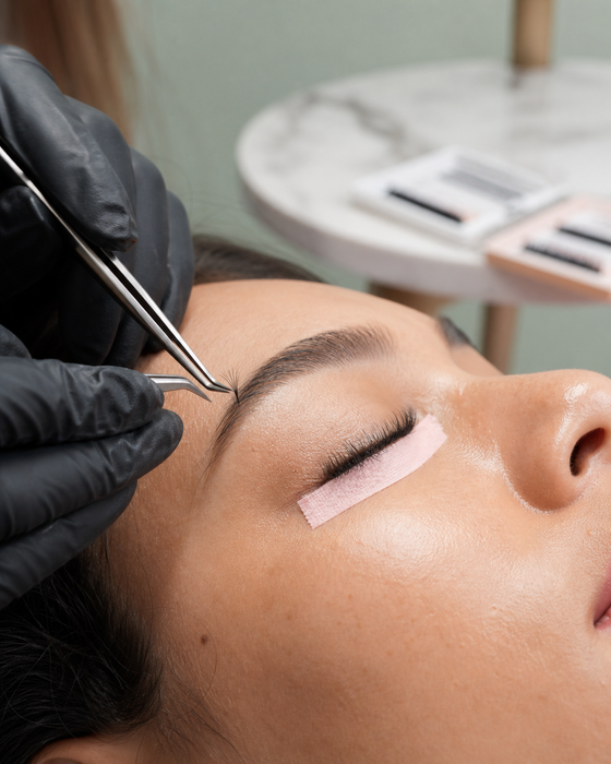 AI-generated ad image: a lash artist's gloved hands applying extensions to a client lying under a ring light in a pastel studio