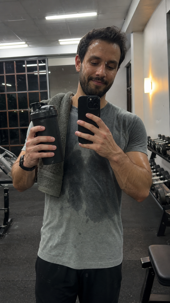 AI-generated creator image: a man in a gym mirror selfie holding a plain shaker bottle, sweaty, fluorescent light, late evening