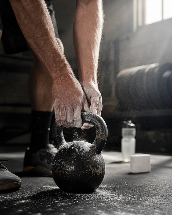 AI-generated ad image: chalked hands gripping a kettlebell on a black gym floor, chalk dust in low light
