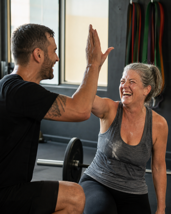 AI-generated ad image: a personal trainer and a client high-fiving after a set, both sweaty and laughing, gym in soft light